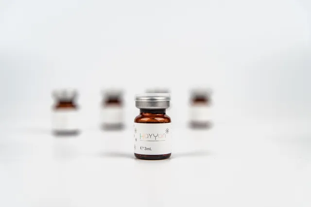 Lọ HAYYAN Solution Essence 3ml với nhãn trắng trên nền trắng, các lọ khác mờ phía sau